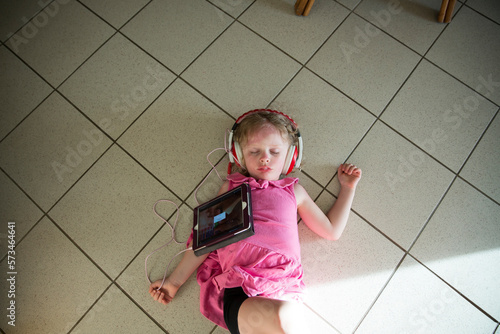 Young Girl Wearing Headphones, Playing iPad, Sleeps on Tile Floor photo
