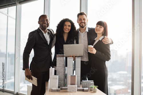 Happy smiling successful diverse multiracial business coworkers, posing on camera during meeting in office room working with city buildings model. Bright people work as urban planners. photo