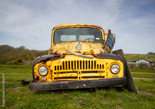 A rusty old antique yellow work truck on the grass