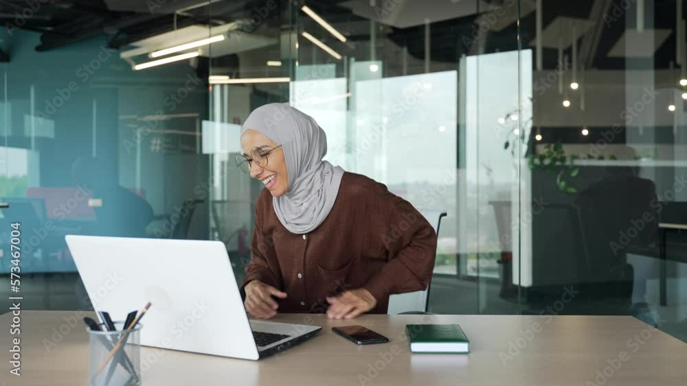 Energetic young muslim businesswoman in hijab feels satisfied with laptop work well done and dancing in the office Happy worker relax after hard working day finished project on computer at workplace Energetic young muslim businesswoman in hijab feels satisfied with laptop work well done and dancing in the office Happy worker relax after hard working day finished project on computer at workplace