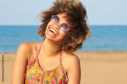 Photos Portrait of cheerful candid girl with frizzy hair in fashionable round sunglasses and brackets wearing summer dress with bare shoulders
