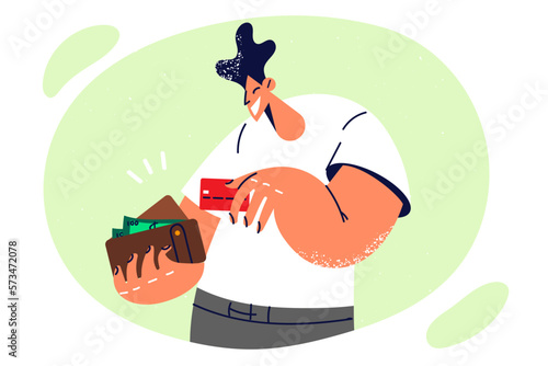 Positive man with wallet filled with banknotes takes out credit card to pay in store after shopping