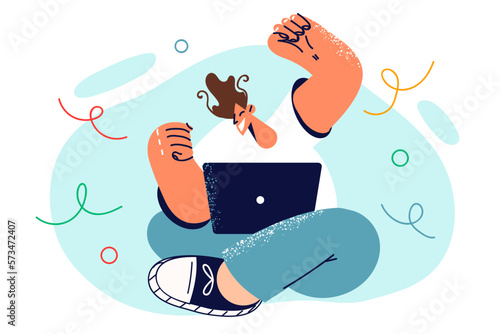 Man raises hands up sitting on floor with laptop on knees celebrating victory in computer game 