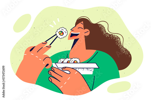 Happy woman with Chinese chopsticks eats rice and fish maki rolls ordered in Japanese restaurant