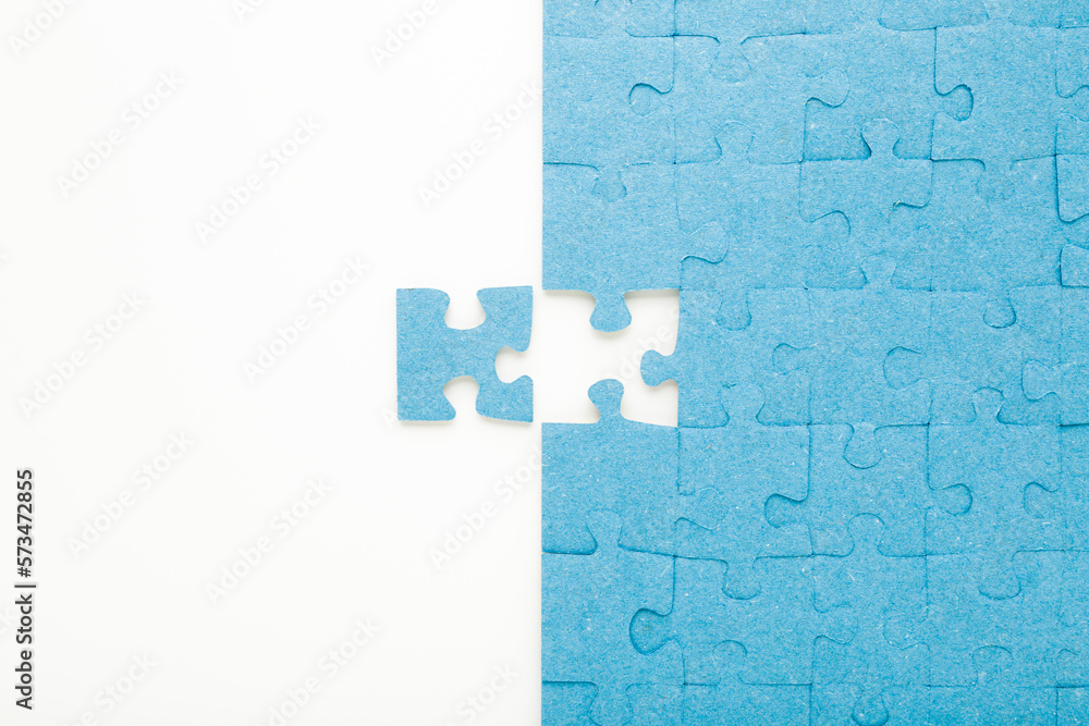 Unfinished blue puzzle with last one piece on white table background. Closeup. Top down view. Unfinished blue puzzle with last one piece on white table background. Closeup. Top down view.
