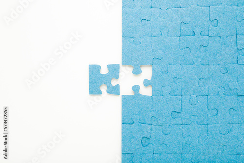 Unfinished blue puzzle with last one piece on white table background. Closeup. Top down view.