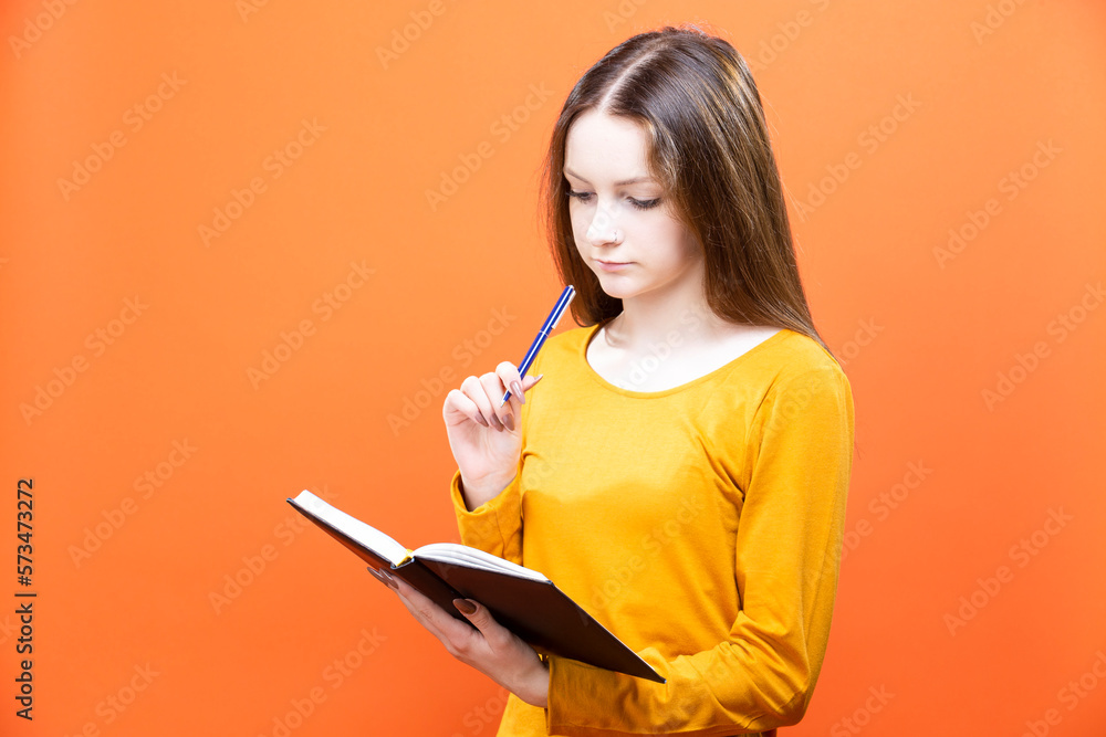 Blond Girl in Yellow Shirt Posing isolated on Orange Background as People Lifestyle Concept While Writing Notes in Notebook Blond Girl in Yellow Shirt Posing isolated on Orange Background as People Lifestyle Concept While Writing Notes in Notebook