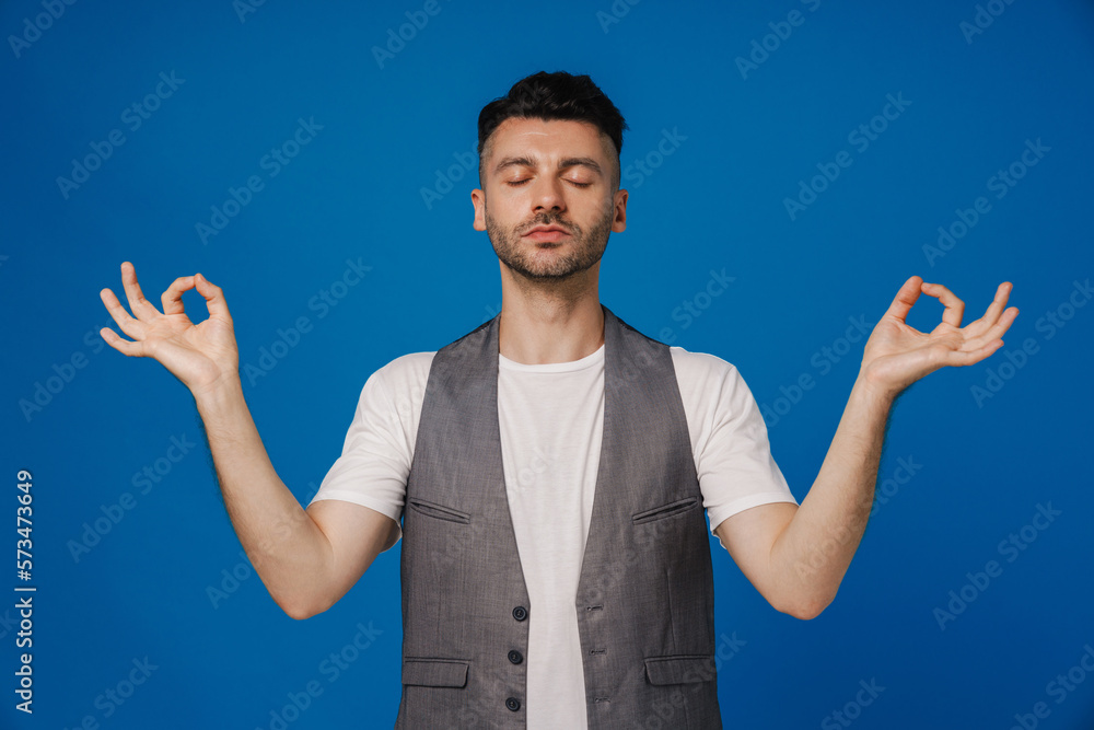 Bearded man meditating with fingers together while standing isolated over blue wall Bearded man meditating with fingers together while standing isolated over blue wall