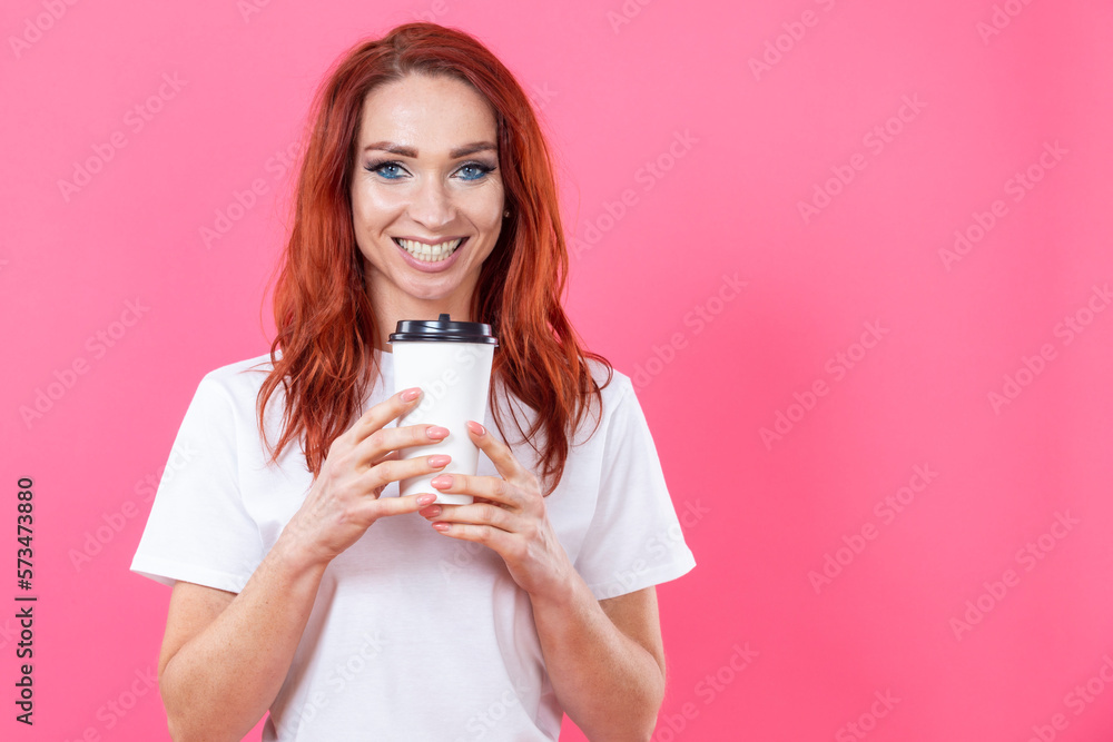 Winsome Female with Ginger Hair Using Disposable Cup of Take Away Coffee, Enjoying Beverage While Wearing White Casual Style Shirt Indoor Studio Shot isolated on pink Winsome Female with Ginger Hair Using Disposable Cup of Take Away Coffee, Enjoying Beverage While Wearing White Casual Style Shirt Indoor Studio Shot isolated on pink