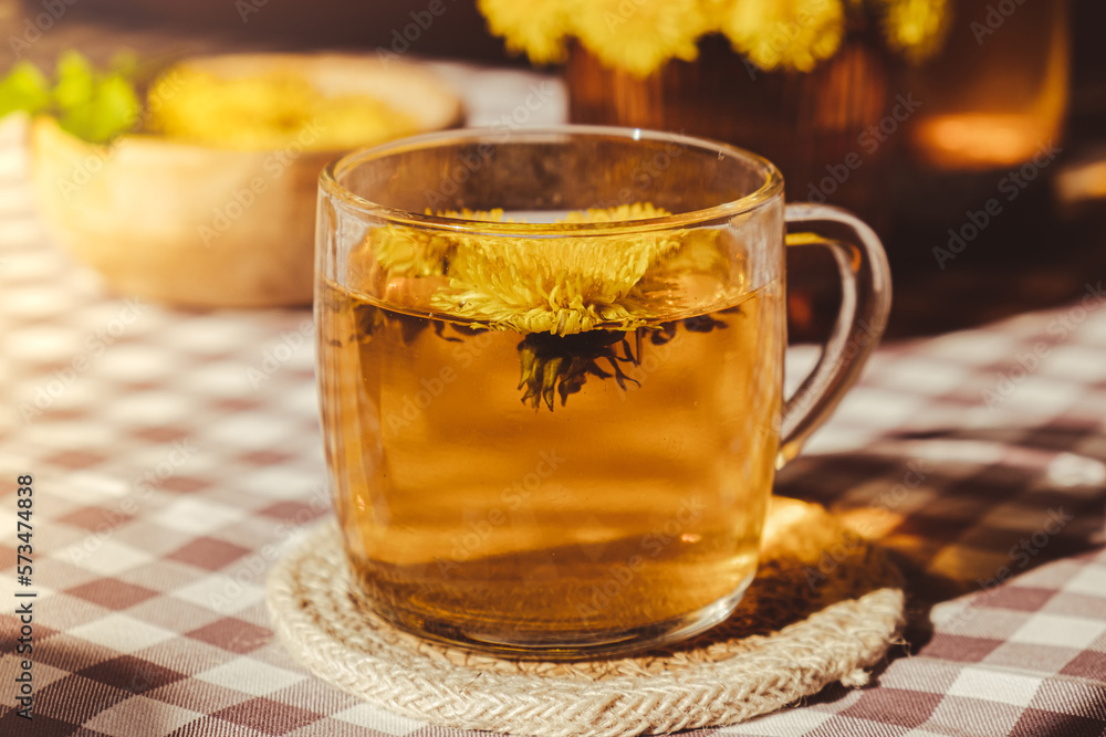 Dandelion flower healthy tea in glass teapot and glass cup on table. Delicious herbal Hot tea from fresh dandelion flowers at home at summer day. Green clearing. Bouquet of dandelions petals Dandelion flower healthy tea in glass teapot and glass cup on table. Delicious herbal Hot tea from fresh dandelion flowers at home at summer day. Green clearing. Bouquet of dandelions petals