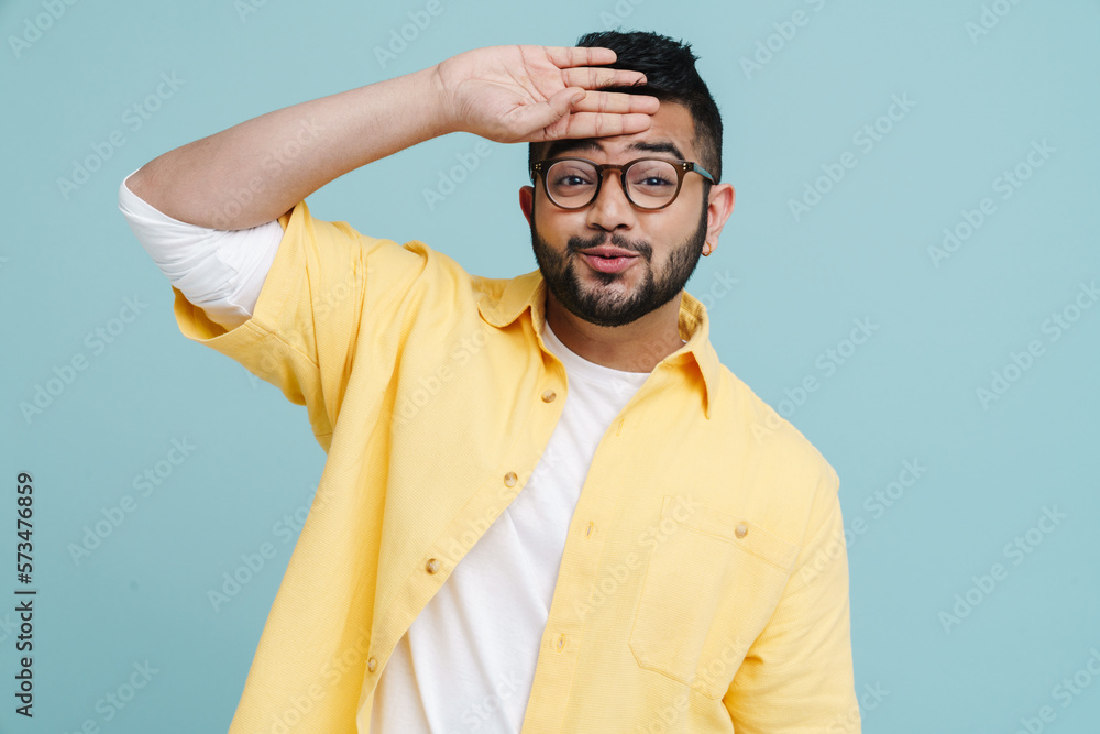Indian man wiping sweat from his forehead standing isolated over blue background Indian man wiping sweat from his forehead standing isolated over blue background