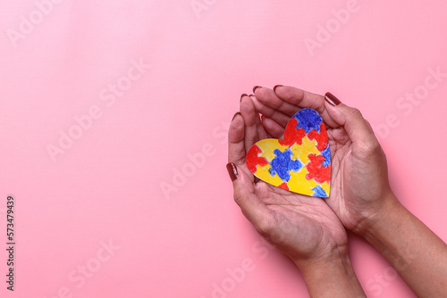 Hands hold colorful puzzle heart shape isolated on pink background with copy space. World Autism Awareness Day.  