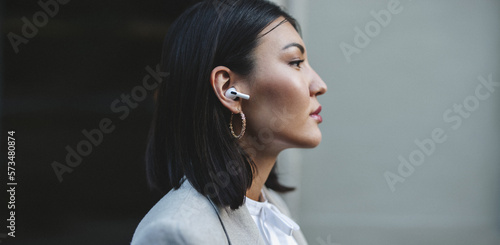 Asian woman listening to music on wireless earphones outdoors