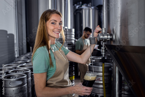 Female brewer working in craft brewery examining quality of the beer.