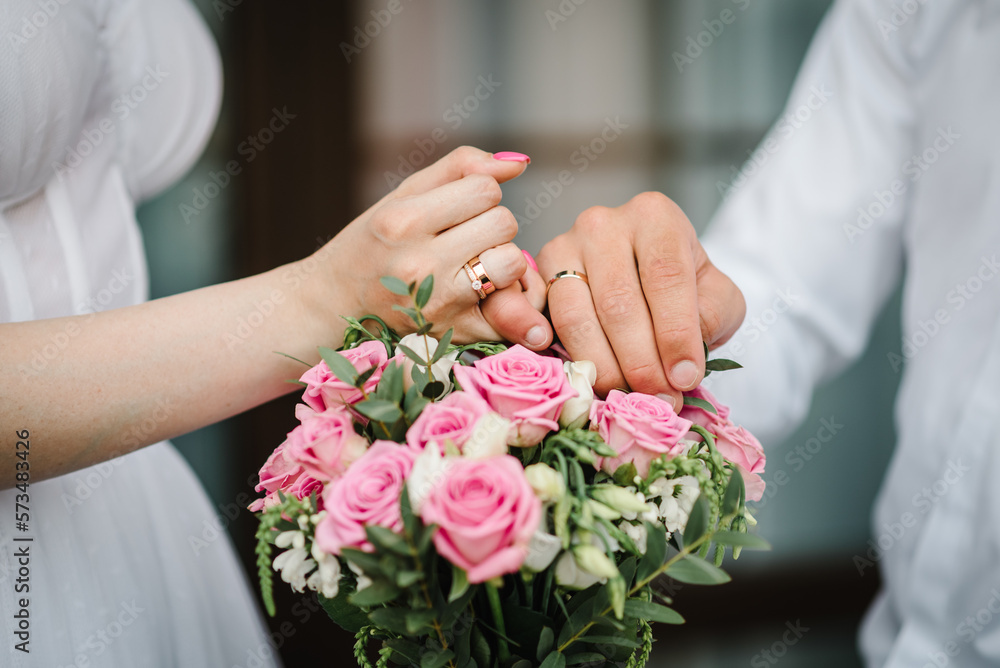Wedding rings on the hands of newlyweds. Cropped image of bride and groom crossing little fingers on bouquet of flowers background. Concept of promise. Linking little fingers to confirm promise. Vow. Wedding rings on the hands of newlyweds. Cropped image of bride and groom crossing little fingers on bouquet of flowers background. Concept of promise. Linking little fingers to confirm promise. Vow.