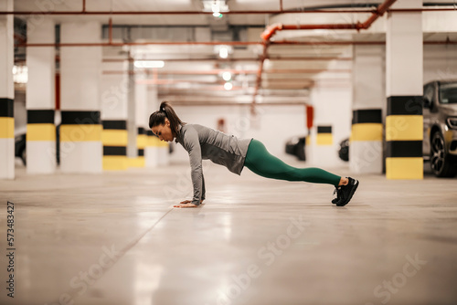 Side view of strong sporty woman doing push ups in underground garage.