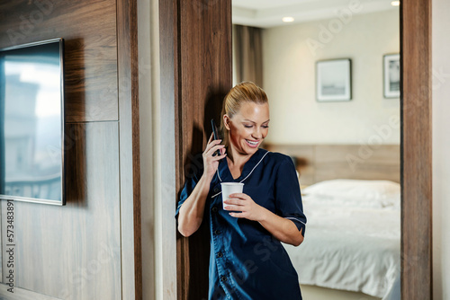 Canvas Print A chambermaid is taking a break while talking on the phone and holding cup of coffee in a hotel room