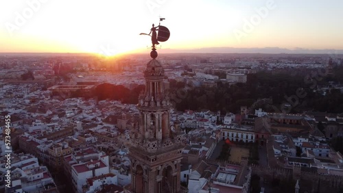 Aerial rotation over the Giraldillo, the sculpture of female form that crowns the Giralda of Seville. Epic sunset behind skyline