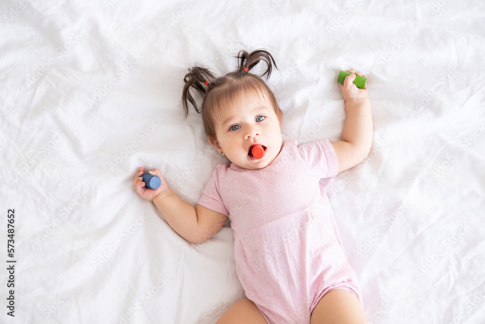 top view of funny baby girl in pink bodysuit playing with children wooden toys on bed top view of funny baby girl in pink bodysuit playing with children wooden toys on bed