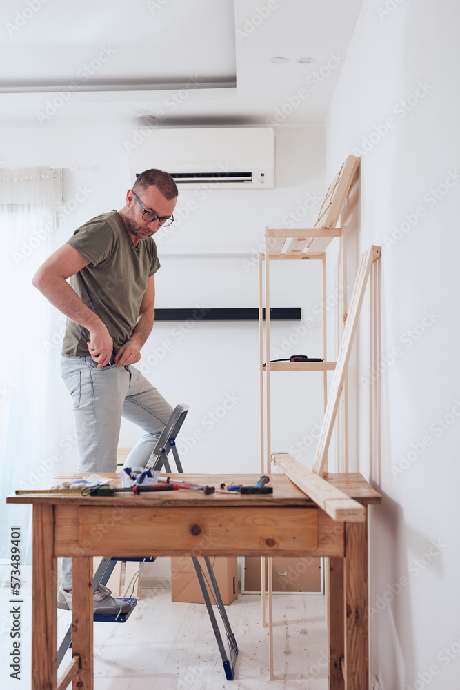 Man assembling new wooden shelf and furniture in the apartment. Man assembling new wooden shelf and furniture in the apartment.
