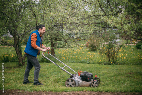 Portrait of a young farmer, gardener with a lawn mower on a plot of land in spring.
