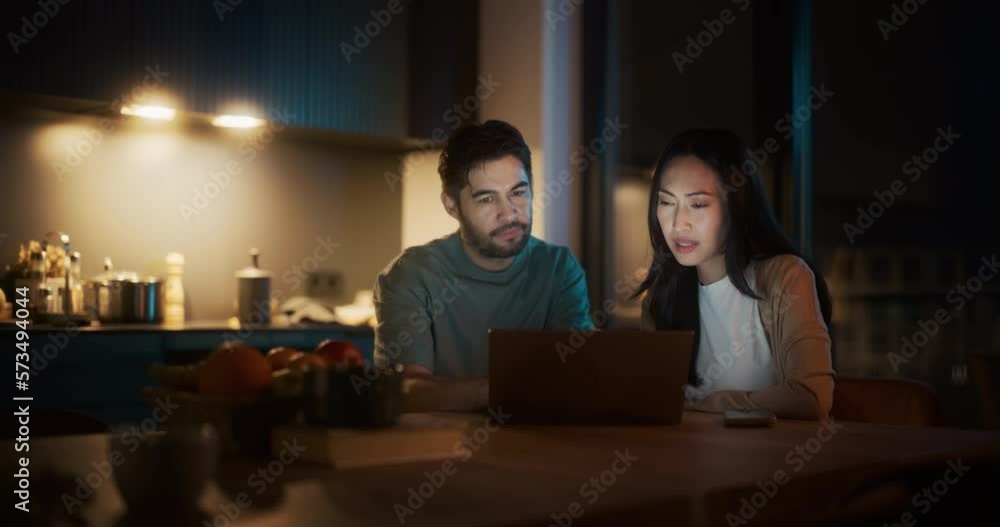 Portrait of Young Couple Using Laptop Computer While Sitting in the Kitchen at Home. Boyfriend and Girlfriend Doing Online Shopping to Renovate the House, Browsing the Internet to Compare Sales Portrait of Young Couple Using Laptop Computer While Sitting in the Kitchen at Home. Boyfriend and Girlfriend Doing Online Shopping to Renovate the House, Browsing the Internet to Compare Sales
