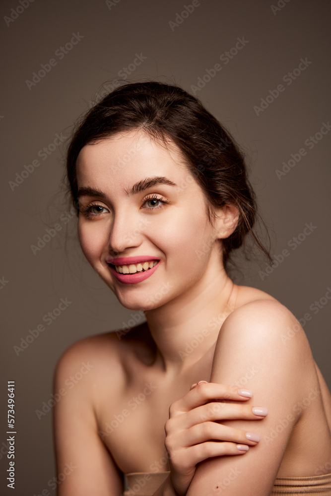 Smiling. Portrait of young beautiful girl with brown hair, pink lipstick makeup posing over dark grey studio background. Concept of natural beauty, skincare, cosmetology, plastic surgery, health Smiling. Portrait of young beautiful girl with brown hair, pink lipstick makeup posing over dark grey studio background. Concept of natural beauty, skincare, cosmetology, plastic surgery, health