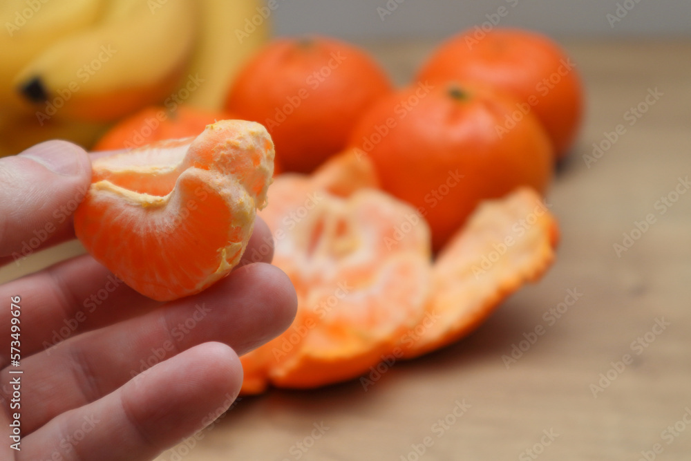 Man with fresh tangerine at table indoors. View from above. Close-up of yummy healthy mandarin fruit. Macro shot of man holding bright orange tangerine on camera.
