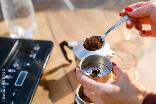 A female hand with spoon of ground coffee is filled with a geyser coffee maker.