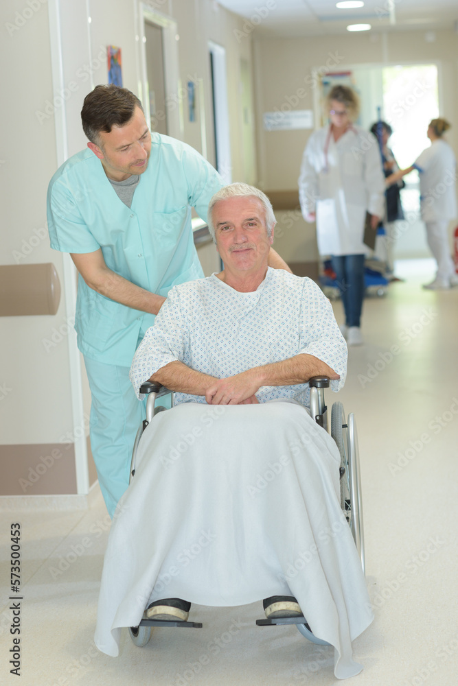 nurse pushing senior patient in wheelchair along corridor nurse pushing senior patient in wheelchair along corridor