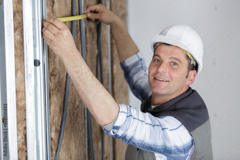 workman measuring wall packed with insulation