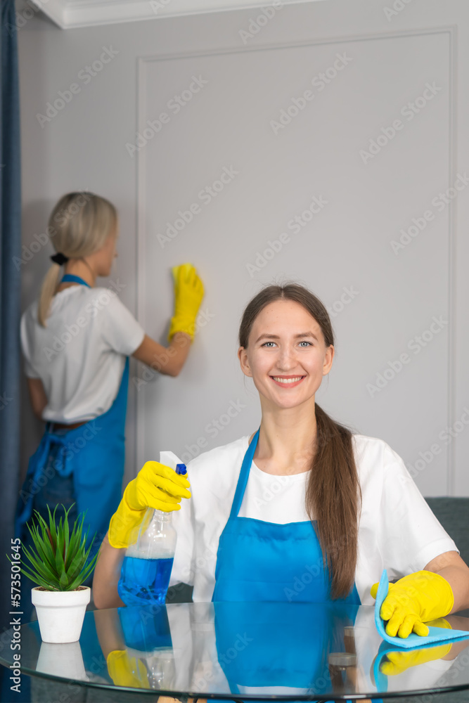Staff of the cleaning service with professional equipment is engaged in cleaning the house, hygiene. Young woman in uniform wipes the table with a cleaning agent, microfiber cloths. Vertical photo Staff of the cleaning service with professional equipment is engaged in cleaning the house, hygiene. Young woman in uniform wipes the table with a cleaning agent, microfiber cloths. Vertical photo