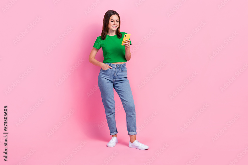 Full length photo of sweet cute lady dressed green t-shirt typing message modern device isolated pink color background Full length photo of sweet cute lady dressed green t-shirt typing message modern device isolated pink color background