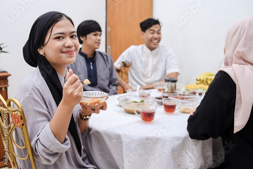 Muslim woman smiles while holding a bowl of dessert to break the fast together in the dining room