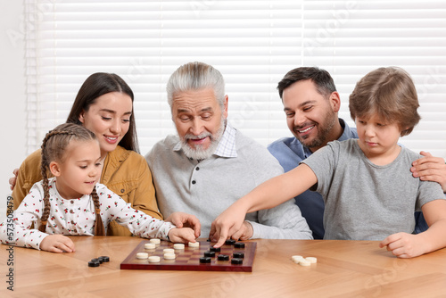 Playing checkers. Parents and grandfather looking at children's game in room
