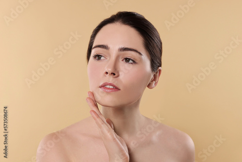 Young woman massaging her face on beige background