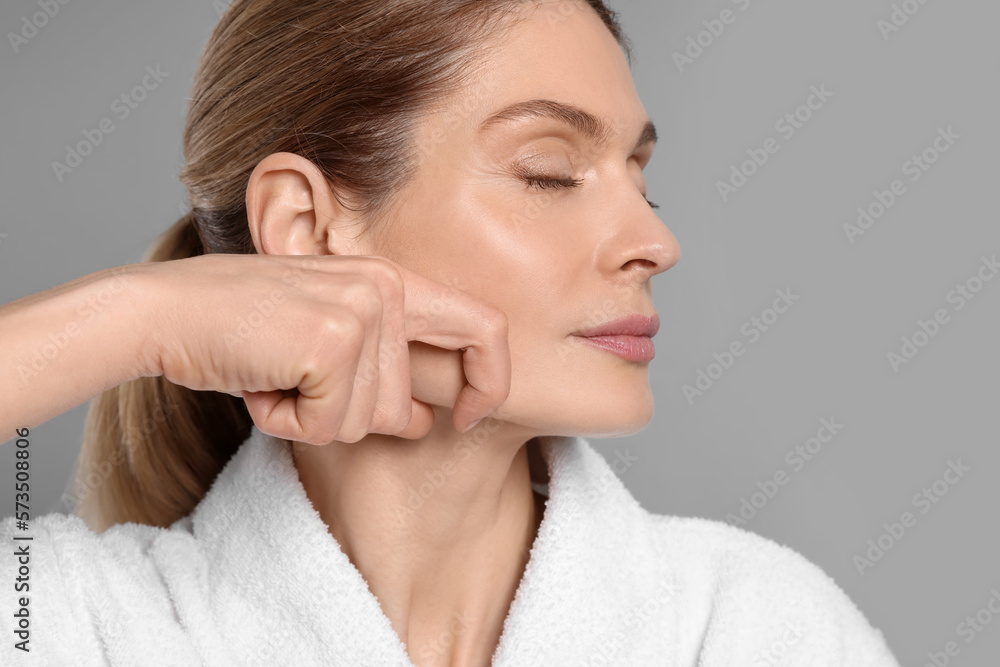 Woman massaging her face on grey background Woman massaging her face on grey background