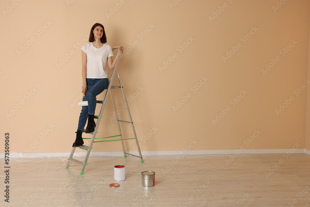 Young woman with roller on metal stepladder indoors. Space for text