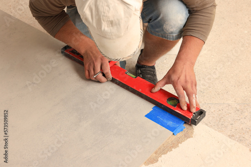 Worker measuring tile with building level indoors