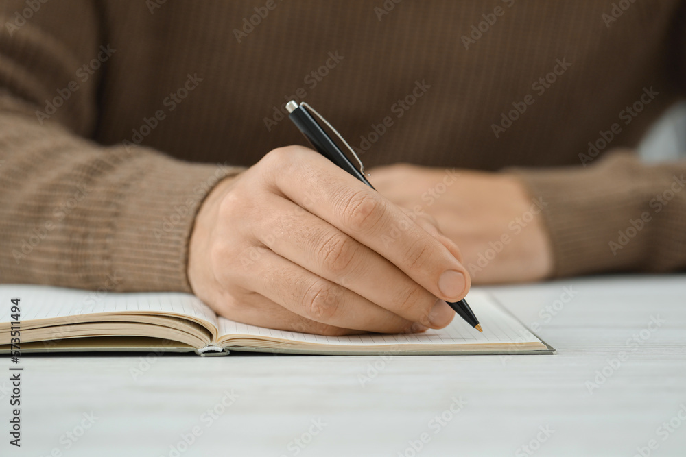 Man writing in notebook at white table, closeup Man writing in notebook at white table, closeup