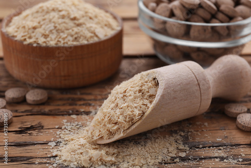 Scoop of brewer`s yeast flakes on wooden table, closeup. Space for text photo