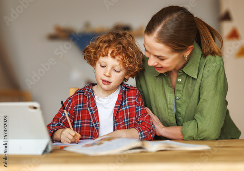 Cheerful mother doing homework with son at home photo