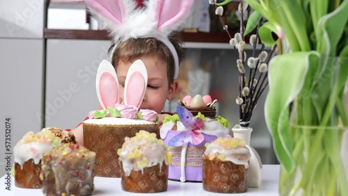 Cute little boy with bunny ears looking at tasty Easter sweet cake, funny kid and happy Easter holidays celebrating. Selective focus