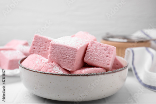 Bowl of delicious sweet marshmallows with powdered sugar on white table, closeup