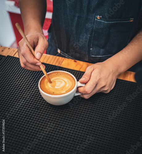 Close-up of the hand of a barista with a wooden spoon making or preparing coffee foam in a cup of coffee.barista making coffee