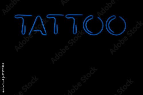blue illuminated tattoo sign in a shop window. Close-up image. Tattoo Studio. isolated on black background. night scene. empty copy space for inscription.