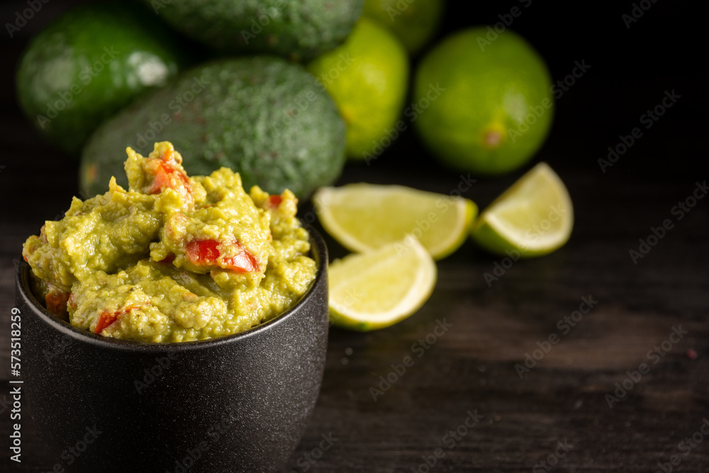 Top view of black jar with guacamole on dark table with sliced limes and avocados, horizontal, selective focus, with copy space Top view of black jar with guacamole on dark table with sliced limes and avocados, horizontal, selective focus, with copy space