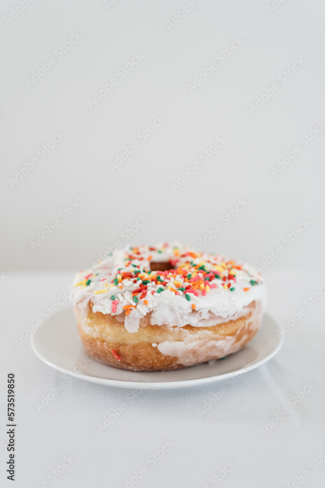 closeup of donut with sprinkles and white icing with a white backdrop closeup of donut with sprinkles and white icing with a white backdrop