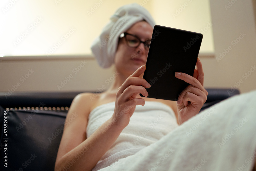 Young girl with eyeglasses reading an ebook relaxed after showering, beauty routine, at home Young girl with eyeglasses reading an ebook relaxed after showering, beauty routine, at home