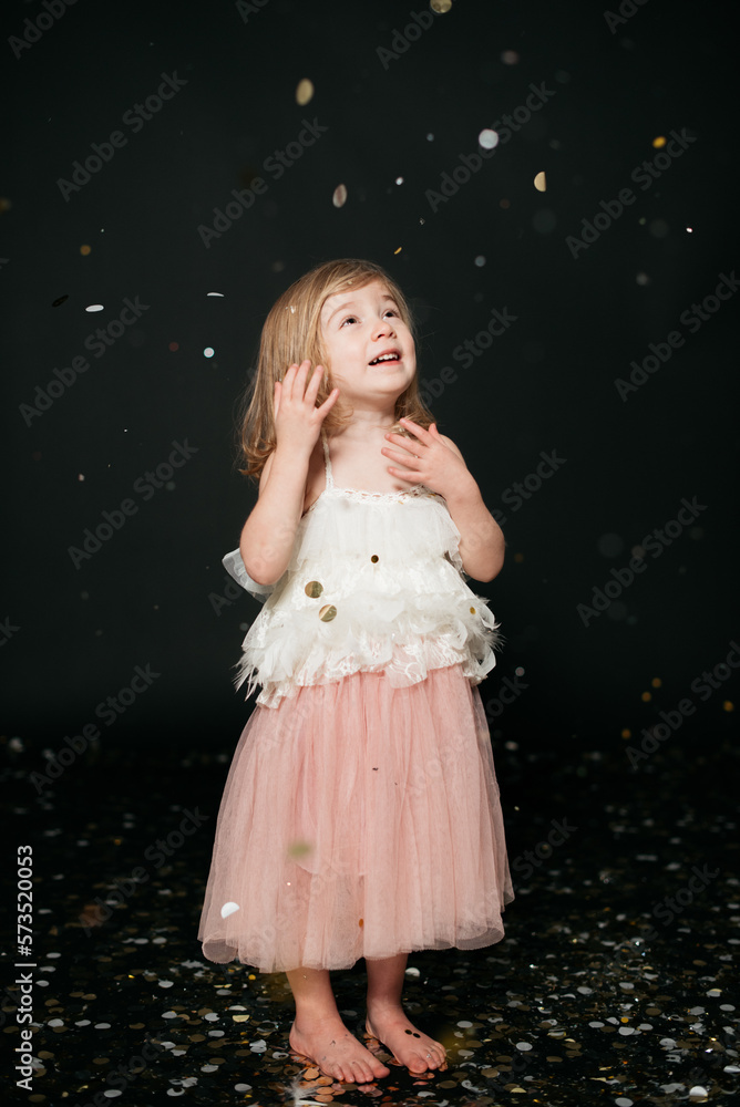 Little girl smiling playing with confetti and black background Little girl smiling playing with confetti and black background